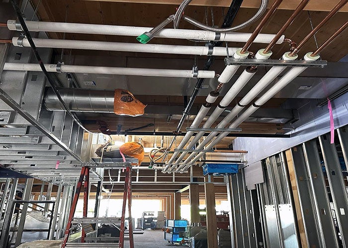 looking up to a ceiling with metal framing, and pipes and wiring roughed in