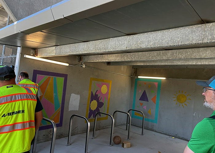 a covered area with bike racks and painted murals with workers in safety vests