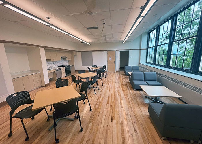 a staff lounge with tables and chairs, stove, and refinished wood floors