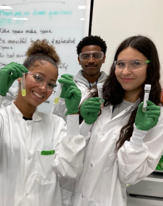three students holding beakers and wearing PPE