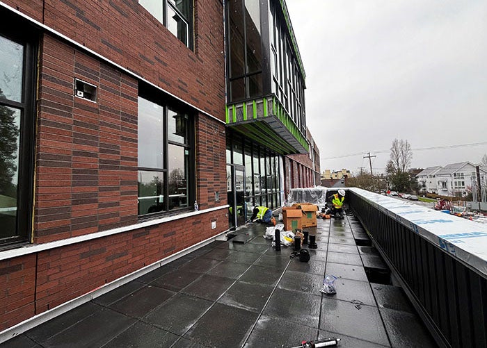 part of a brick building with windows. there are pavers and a wall in front of it.