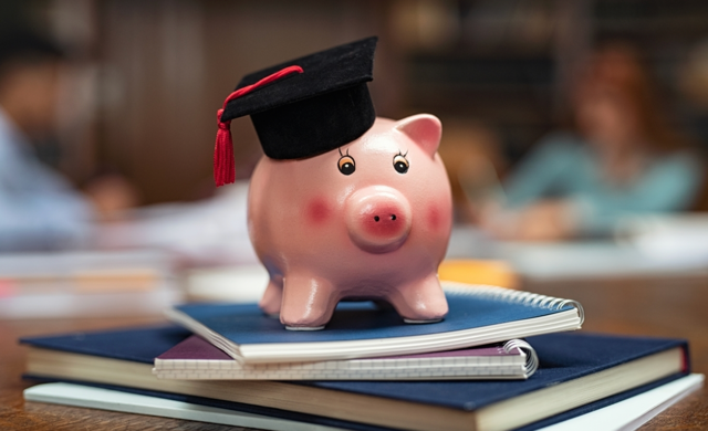 Piggy Bank with Graduation Cap sitting on Diplomas.