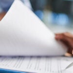 Hand and pen completing paperwork at desk banner