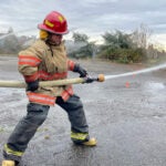 A student in firefighter gear holds a water hose during a training