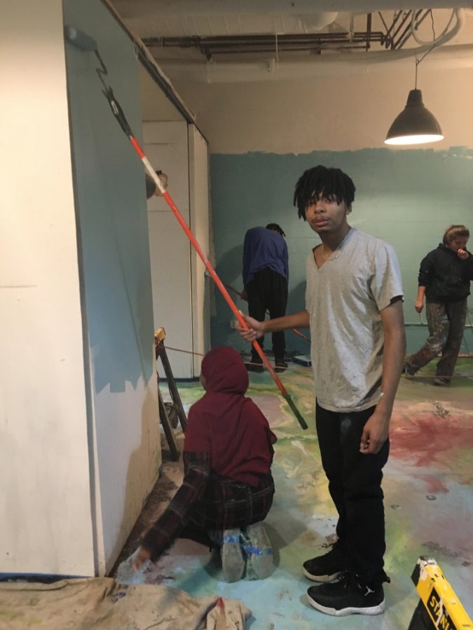 Student panting wall with long handled roller