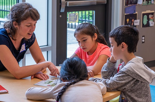 A teacher talks with three young students at a table.