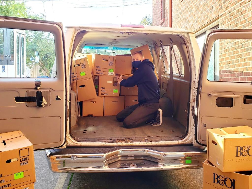 Photo of student wearing mask in back of van with boxes