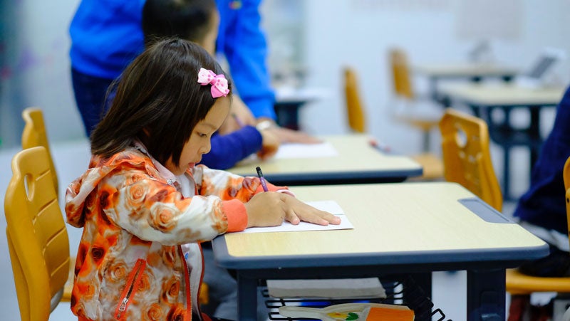 A young student sits at a desk with a pencil in her hand.