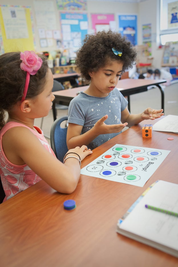 Two young students sit at a desk in a classroom with a math project.