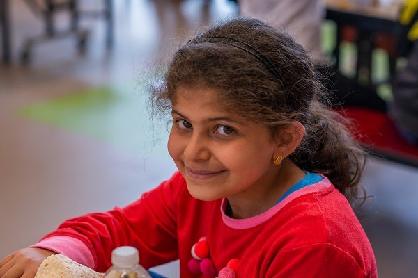 A girl smiles at the camera while eating lunch at school