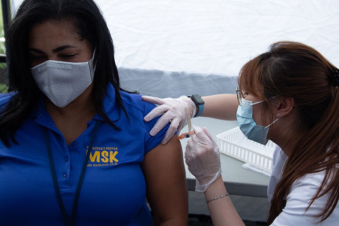 A woman in a mask receives a vaccine dose from a health care provider.
