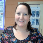 A smiling woman stands in front of a classroom.