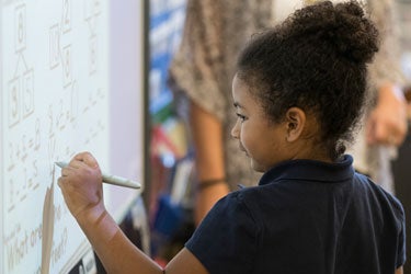 A young student works at a white board in a classroom