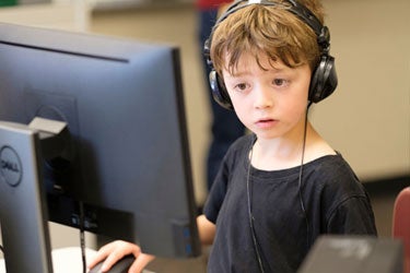 A young student sits at a computer with headphones