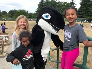 Three students stand together with a school mascot Orca