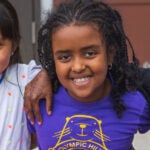 Five elementary students sit together in a courtyard and smile for a photo