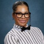 A teacher smiles in front of a blue background