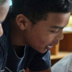 Three middle school age students talk together in a classroom.