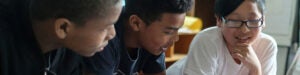 Three middle school age students talk together in a classroom.