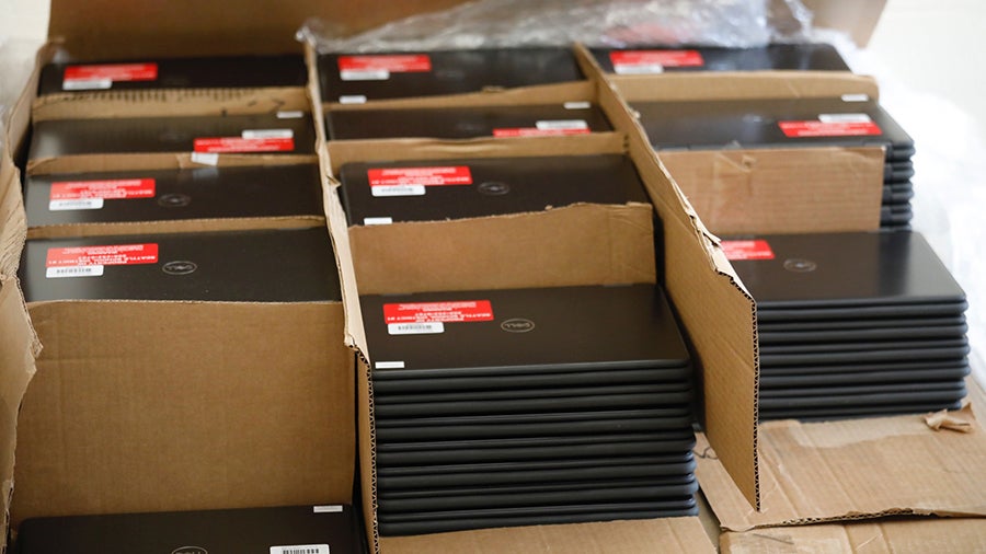 A collection of laptops with SPS stickers are stacked together in boxes on a table