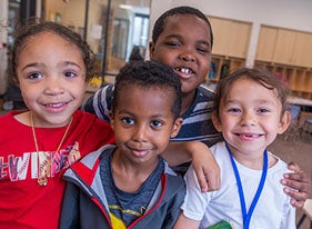 Four young students smile for a photo in a classroom.