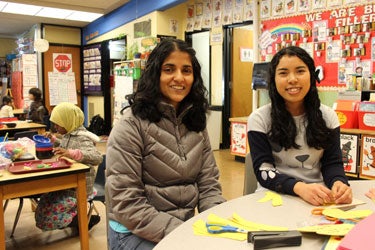 Two volunteers smile for a photo in a classroom