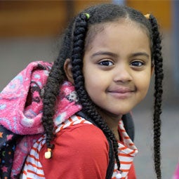 A young student in a classroom smiles for a photo