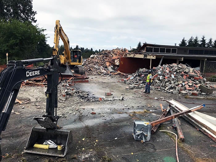 a demolition site with heavy equipment and piles of debris in front of a partially demolished building