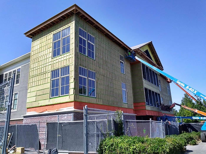 siding being installed on a 3-story building by a person in a lift