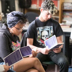 Students sit together in a classroom reading the same book.
