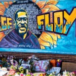 A mural of George Floyd with flowers and memorial in front of the wall.