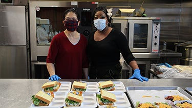Two cafeteria supervisors pose for a photo together in a lunch room.
