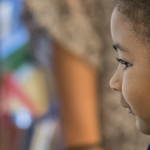 A young student works on a math problem while standing at a white board in a classroom.