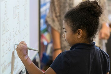 Young student works at a math problem at a white board in a classroom