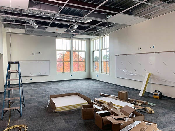a classroom with white boards and carpet installed and the ceiling tiles stacked on the floor
