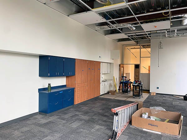 a classroom space that has carpet and some cabinets installed with the ceiling grid still empty