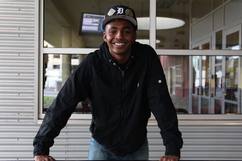 A high school student smiles for a photo in front of a window