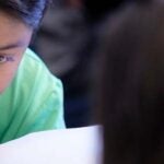 A young student writes with a pencil in a classroom at a desk