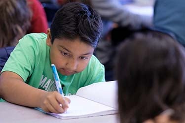 A elementary student writes in a notebook in a classroom