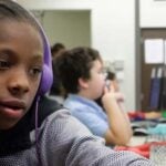 Two older elementary students in a computer lab talk and look at a monitor together