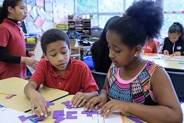 Two students work together at a desk in a clasroom
