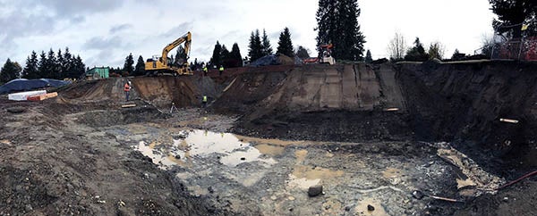 a large pit with puddles in mud is below a wall of dirt