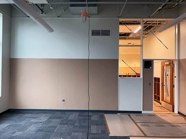 a wall in a classroom has a brown material on the lower half and white paint on the upper half