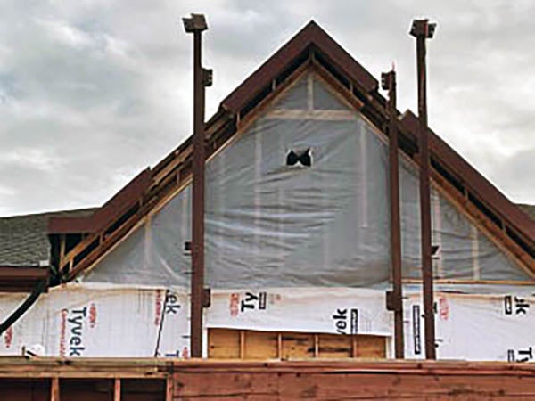 a peaked roof of a building has plastic protecting the interior and steel columns in front of it