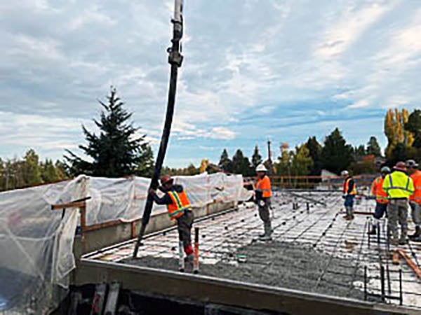 concrete is being pumped into framing with workers guiding the nozzle