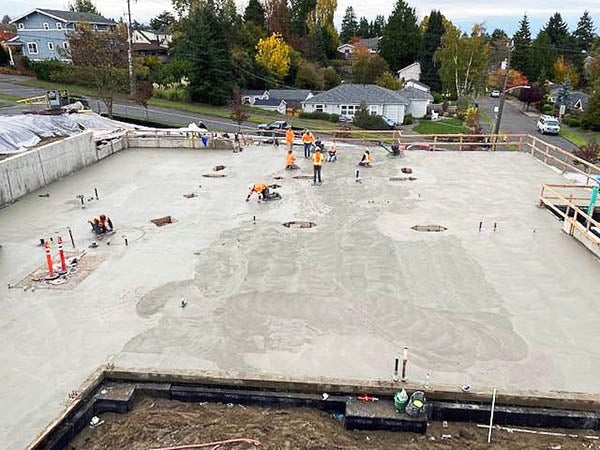 a large area of wet concrete with people working to smooth it out