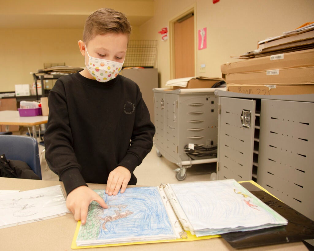 Mark in a school classroom flips through a portfolio of art