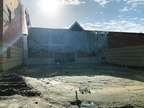 a brick building with part of it draped in plastic with dirt in front of it