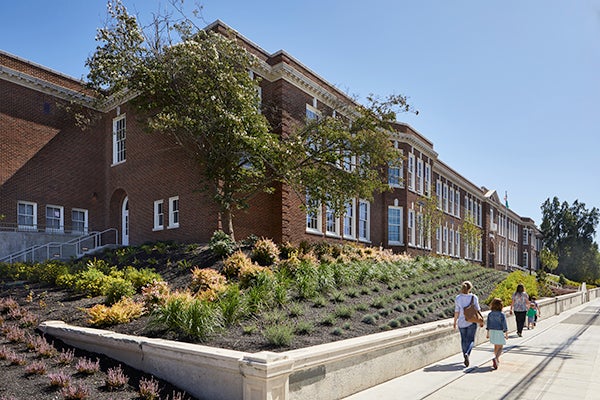 a brick building from the corner. it sits on a hill with gardens around it and a sidewalk goes past