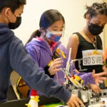 A group of older elementary students work together in a classroom on robotic projects
